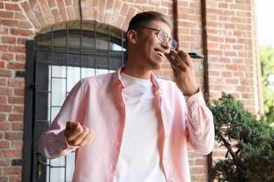 Photo of Young man recording voice message via smartphone outdoors