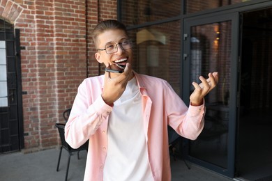 Young man recording voice message via smartphone outdoors