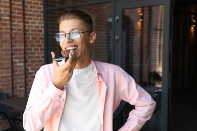 Young man recording voice message via smartphone outdoors