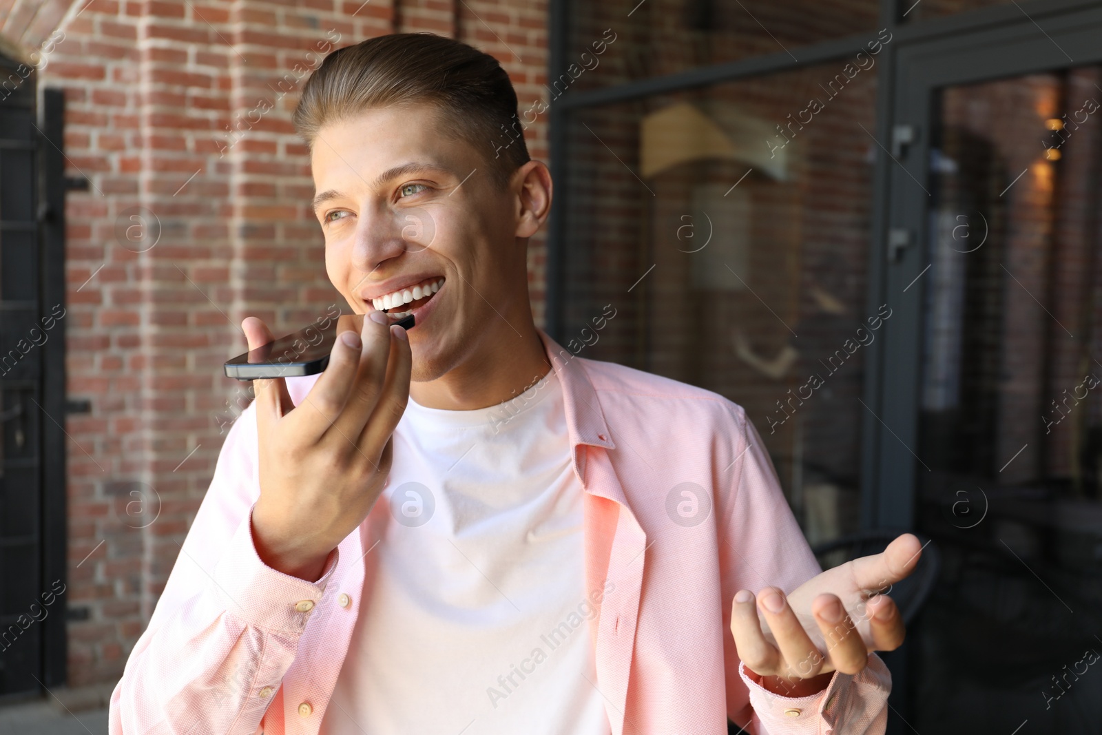 Photo of Young man recording voice message via smartphone outdoors