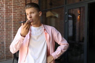 Photo of Young man recording voice message via smartphone outdoors