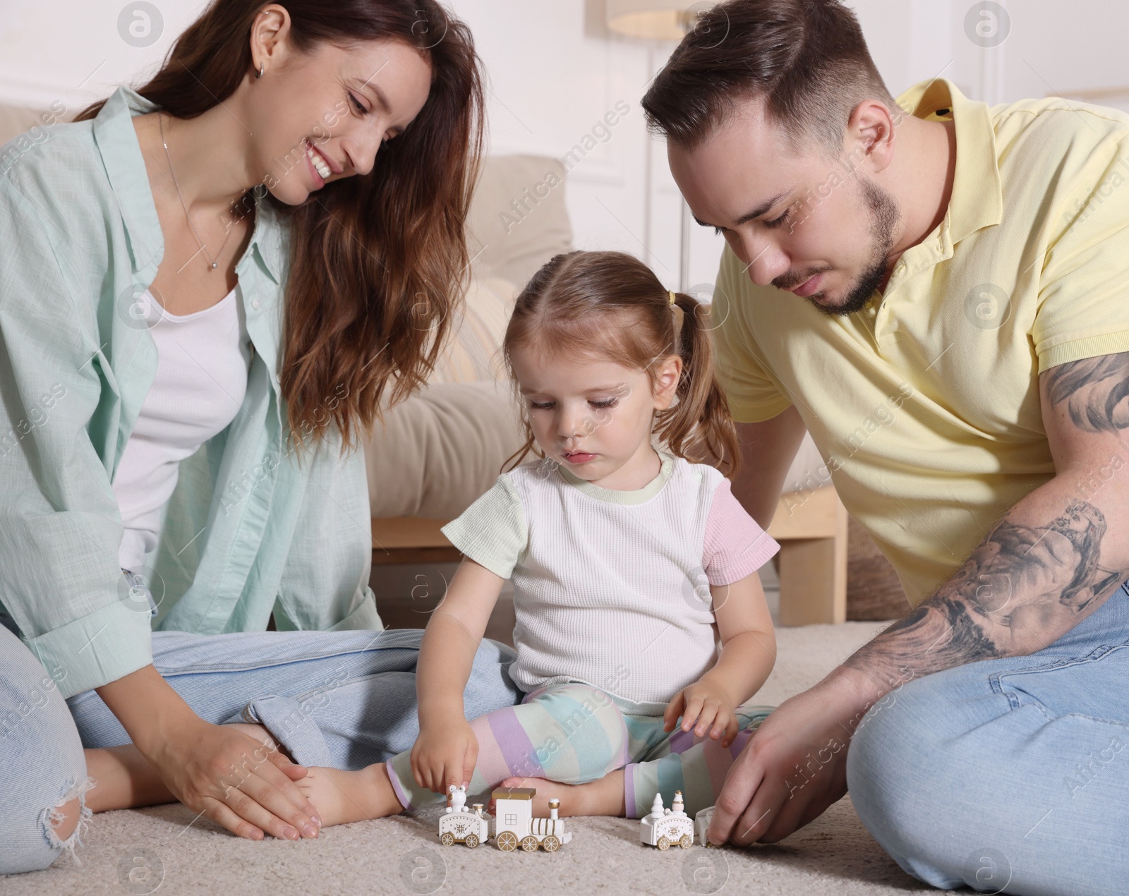 Photo of Happy family. Parents and their cute little daughter playing with toy train at home