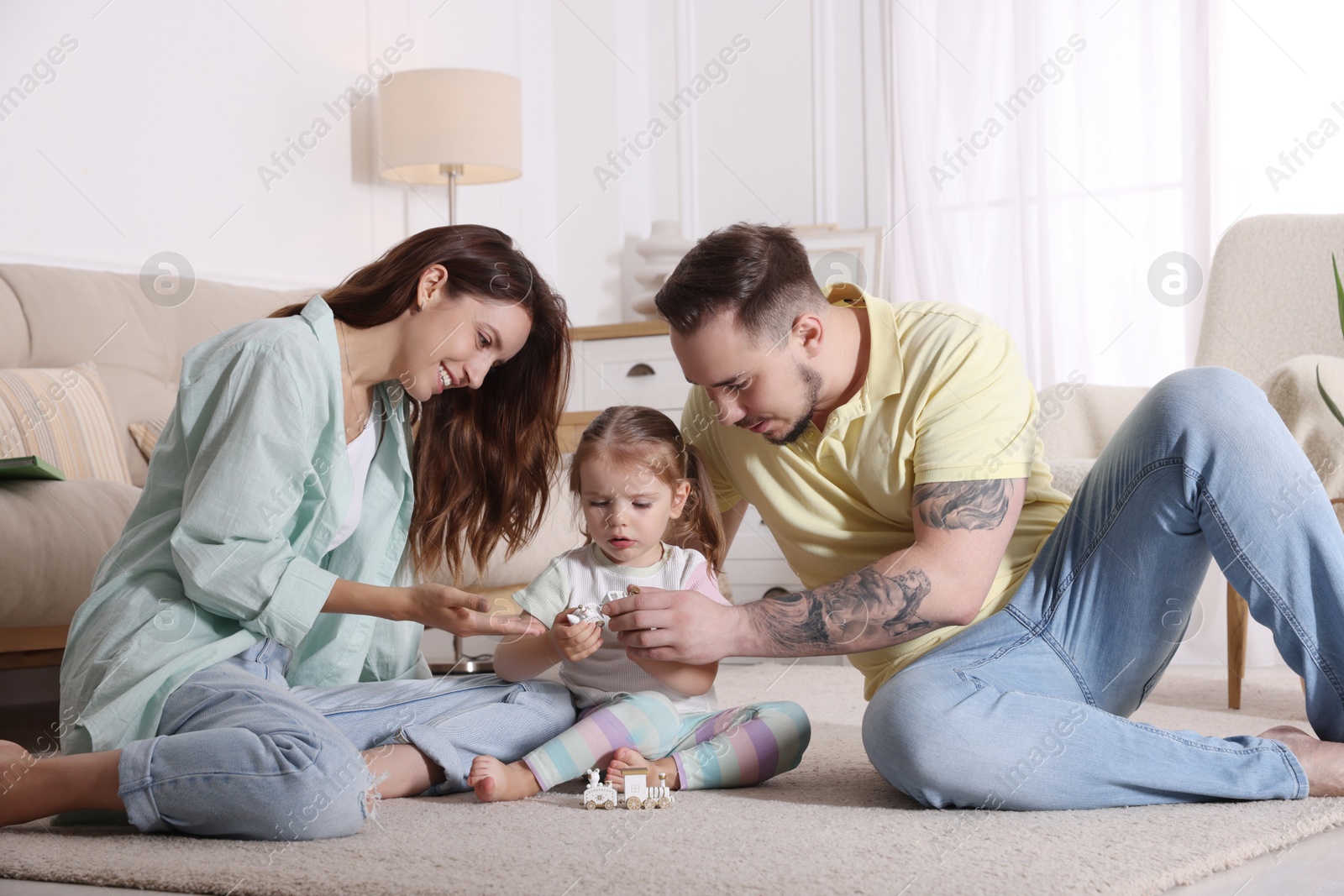 Photo of Happy family. Parents and their cute little daughter playing with toy train at home