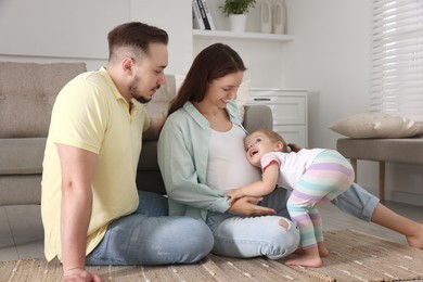 Happy family. Pregnant woman, her husband and cute little daughter at home