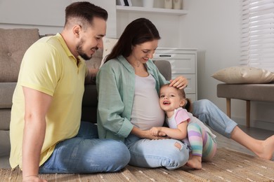 Photo of Happy family. Pregnant woman, her husband and cute little daughter at home