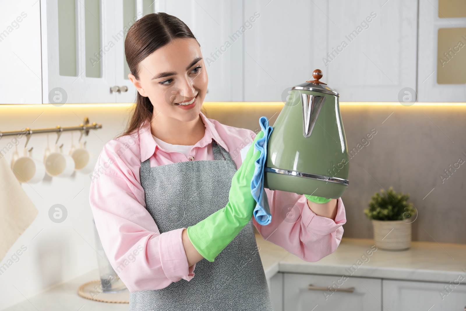 Photo of Beautiful young woman wiping kettle with rag in kitchen