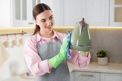 Photo of Beautiful young woman wiping kettle with rag in kitchen