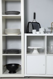 Shelving unit and storage cabinet with kitchenware near grey wall indoors