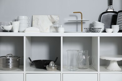 Shelving unit with kitchenware near grey wall indoors