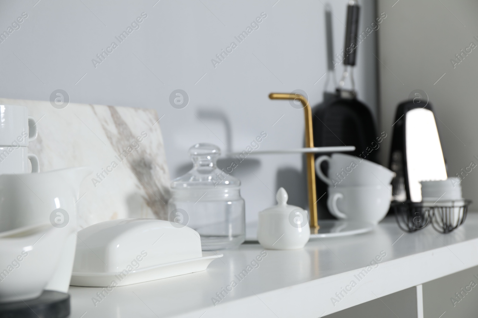 Photo of Different kitchenware on white shelf near grey wall indoors, closeup