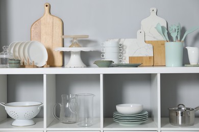 Shelving unit with kitchenware near grey wall indoors