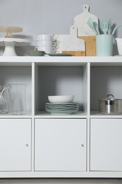 Shelving unit and storage cabinet with kitchenware near grey wall indoors