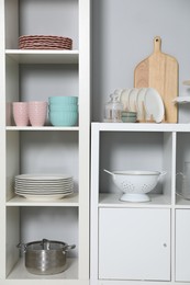 Shelving unit and storage cabinet with kitchenware near grey wall indoors