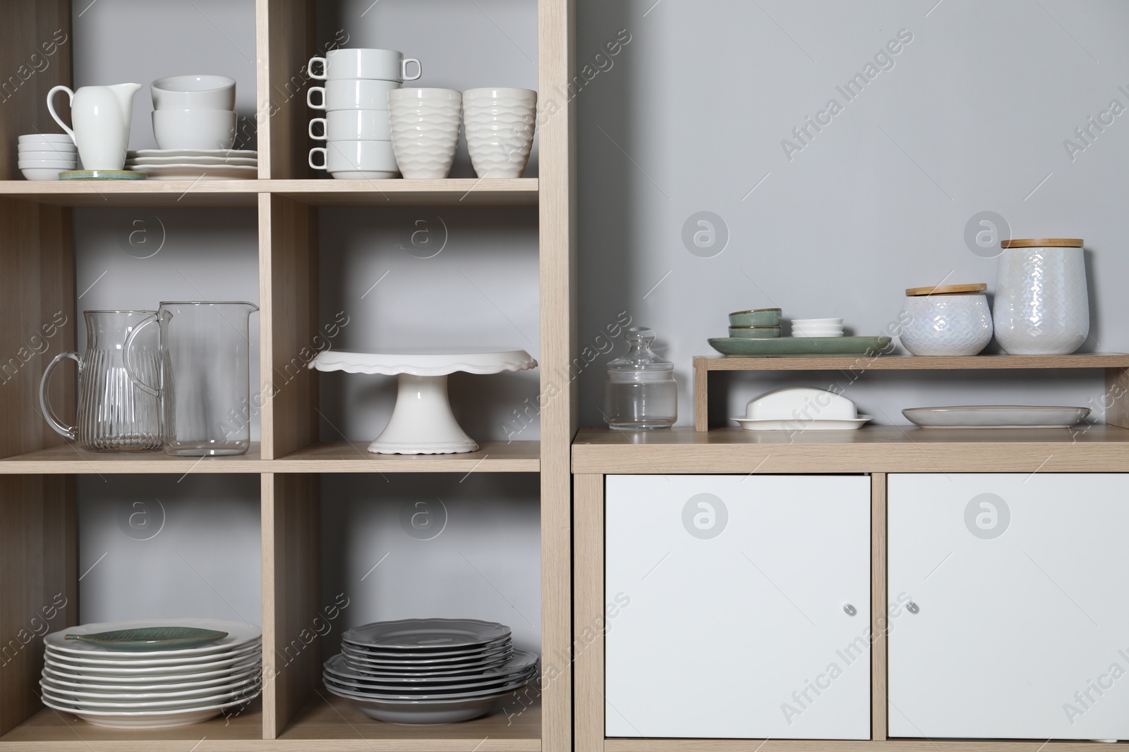 Photo of Wooden shelving unit and storage cabinet with kitchenware near grey wall indoors