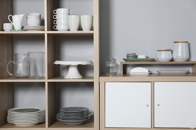 Wooden shelving unit and storage cabinet with kitchenware near grey wall indoors