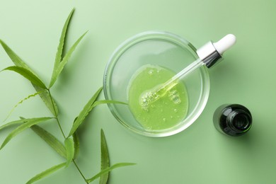 Photo of Petri dish with cosmetic product, bottle, pipette and leaves on green background, flat lay