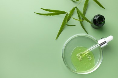 Photo of Petri dish with cosmetic product, bottle, pipette and leaves on green background, flat lay. Space for text