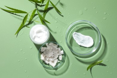 Petri dishes with cosmetic products and leaves on green background, flat lay