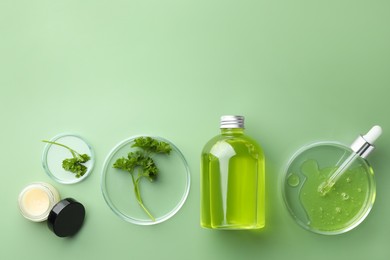 Photo of Petri dishes with cosmetic products, pipette and parsley on green background, flat lay. Space for text