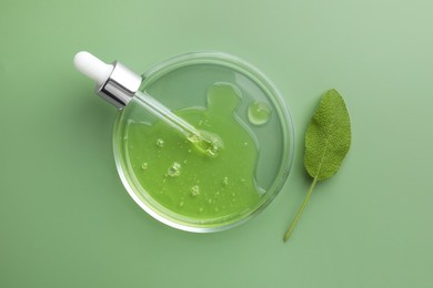 Photo of Petri dish with cosmetic product, pipette and leaf on green background, flat lay