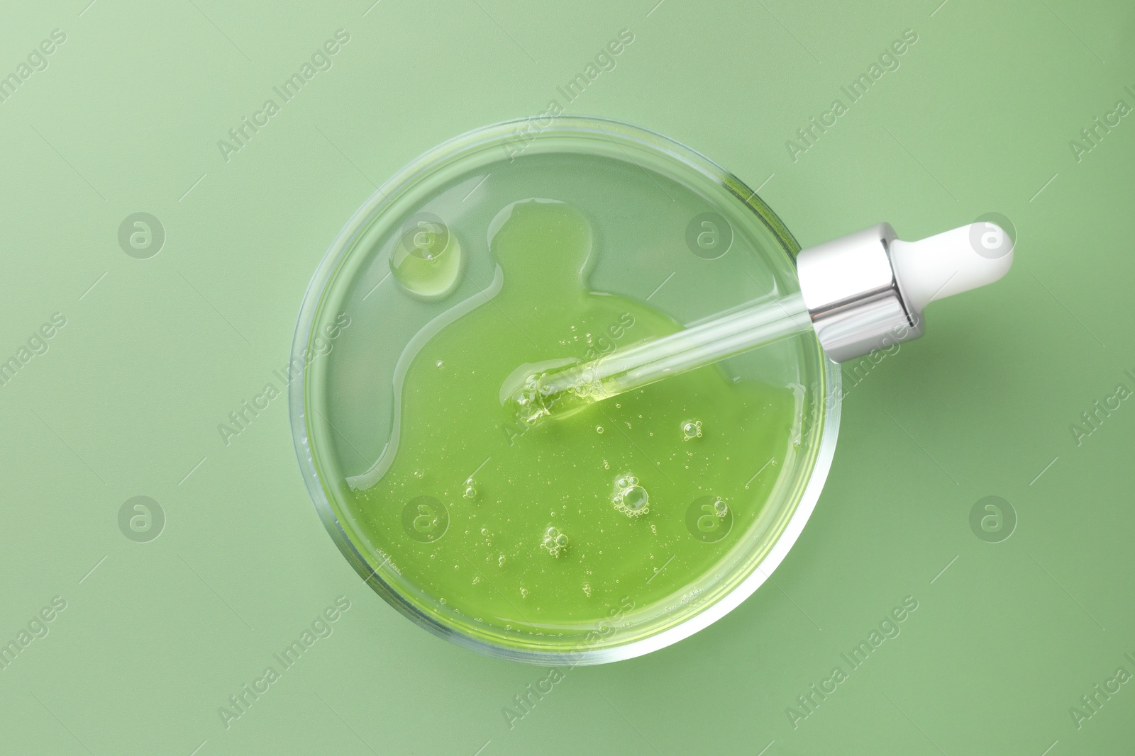 Photo of Petri dish with cosmetic product and pipette on green background, top view