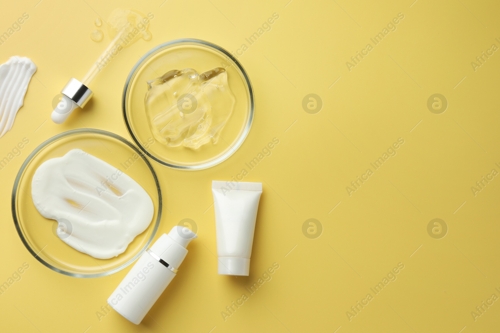 Photo of Petri dishes with cosmetic products and pipette on yellow background, flat lay. Space for text