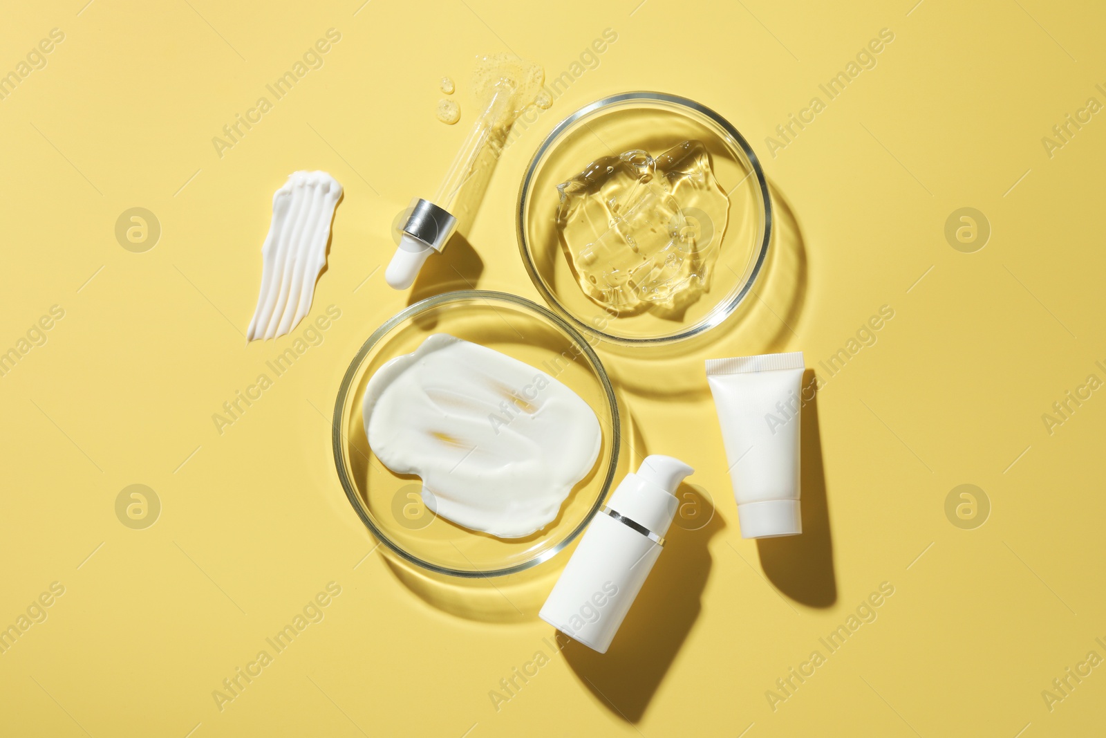 Photo of Petri dishes with cosmetic products and pipette on yellow background, flat lay