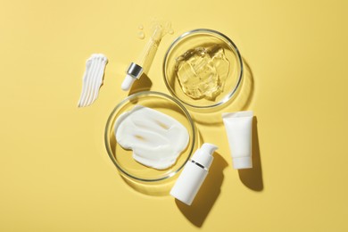 Photo of Petri dishes with cosmetic products and pipette on yellow background, flat lay