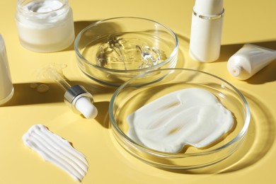 Photo of Petri dishes with cosmetic products and pipette on yellow background, closeup