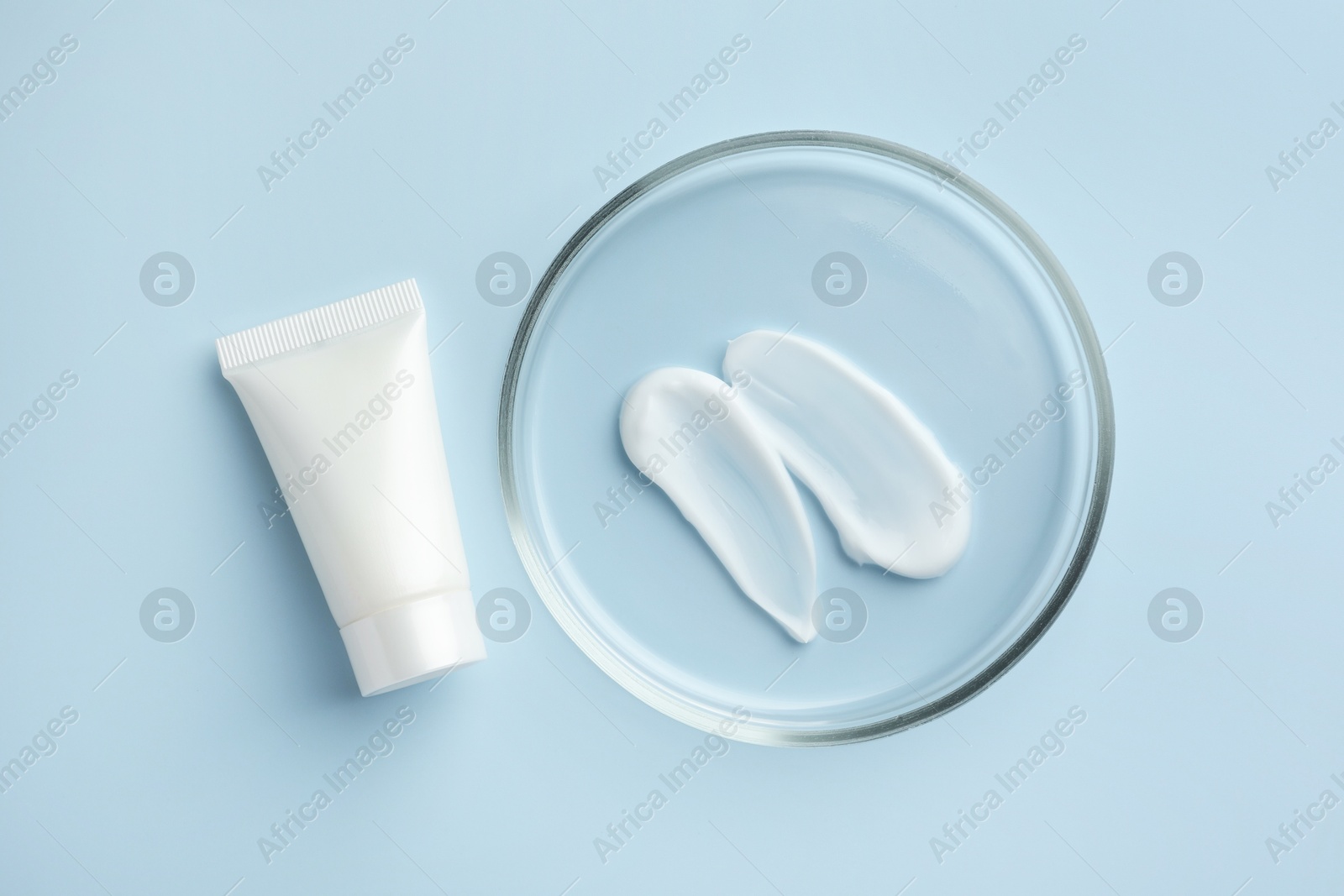 Photo of Petri dish with cosmetic product and tube on light blue background, flat lay