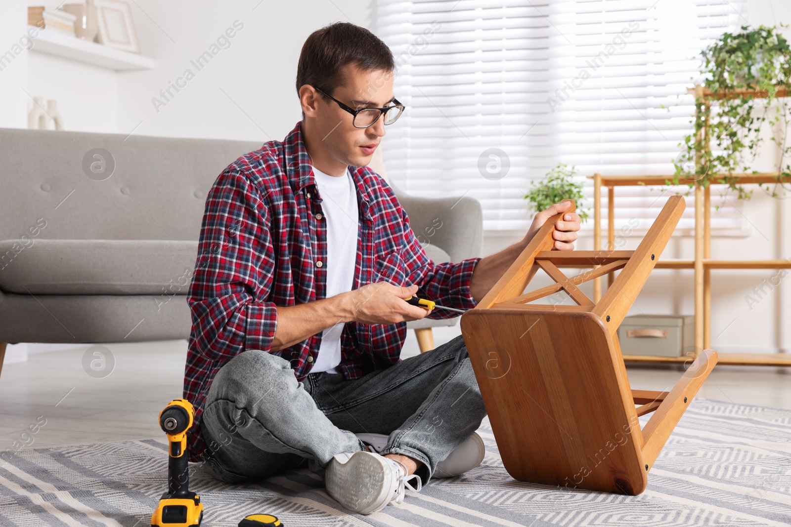 Photo of Man repairing wooden stool with screwdriver indoors