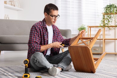 Photo of Man repairing wooden stool with screwdriver indoors