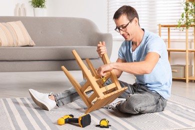 Man repairing wooden stool with screwdriver indoors