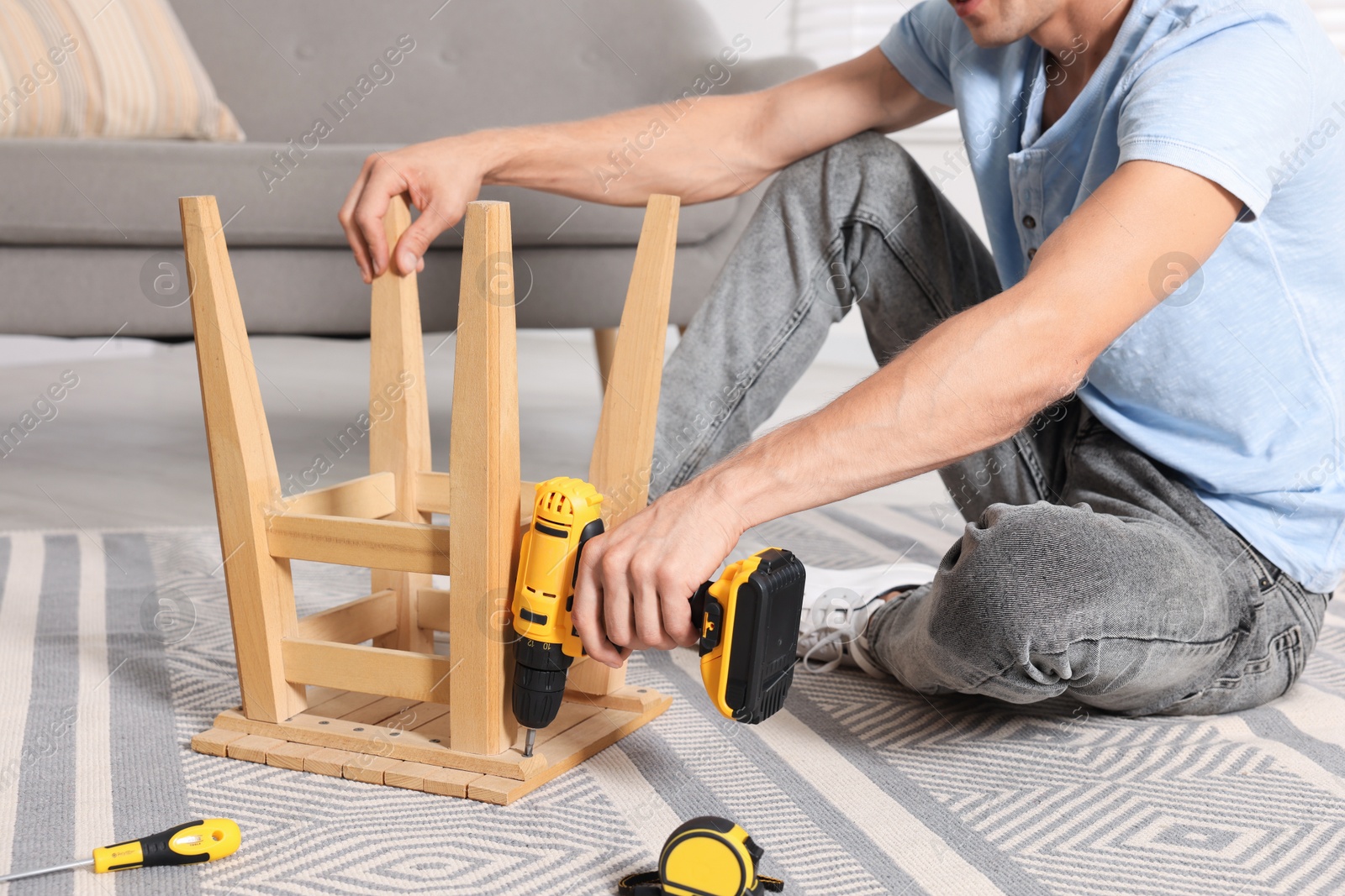 Photo of Man repairing wooden stool with electric screwdriver indoors, closeup