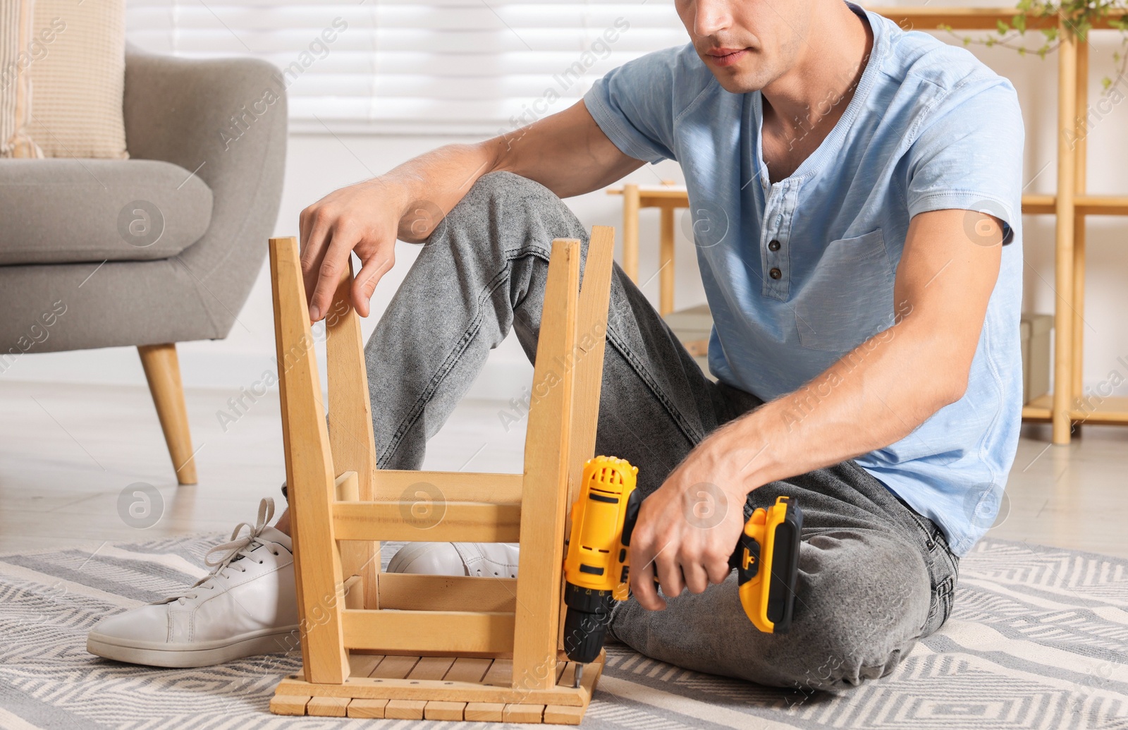 Photo of Man repairing wooden stool with electric screwdriver indoors, closeup