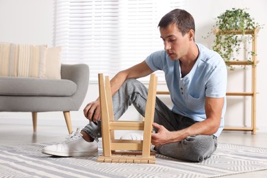 Photo of Man using tape measure while repairing wooden stool indoors