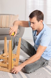 Photo of Man using tape measure while repairing wooden stool indoors