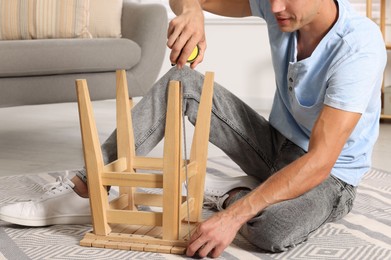 Man using tape measure while repairing wooden stool indoors, closeup