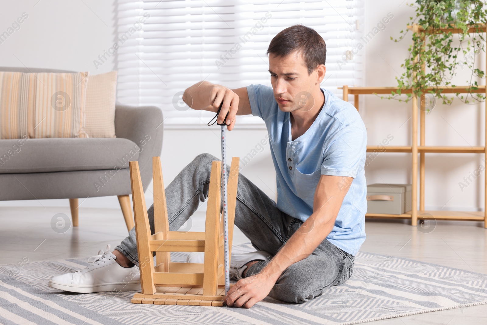 Photo of Man using tape measure while repairing wooden stool indoors