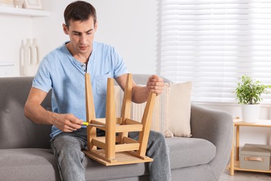 Photo of Man repairing wooden stool with screwdriver indoors