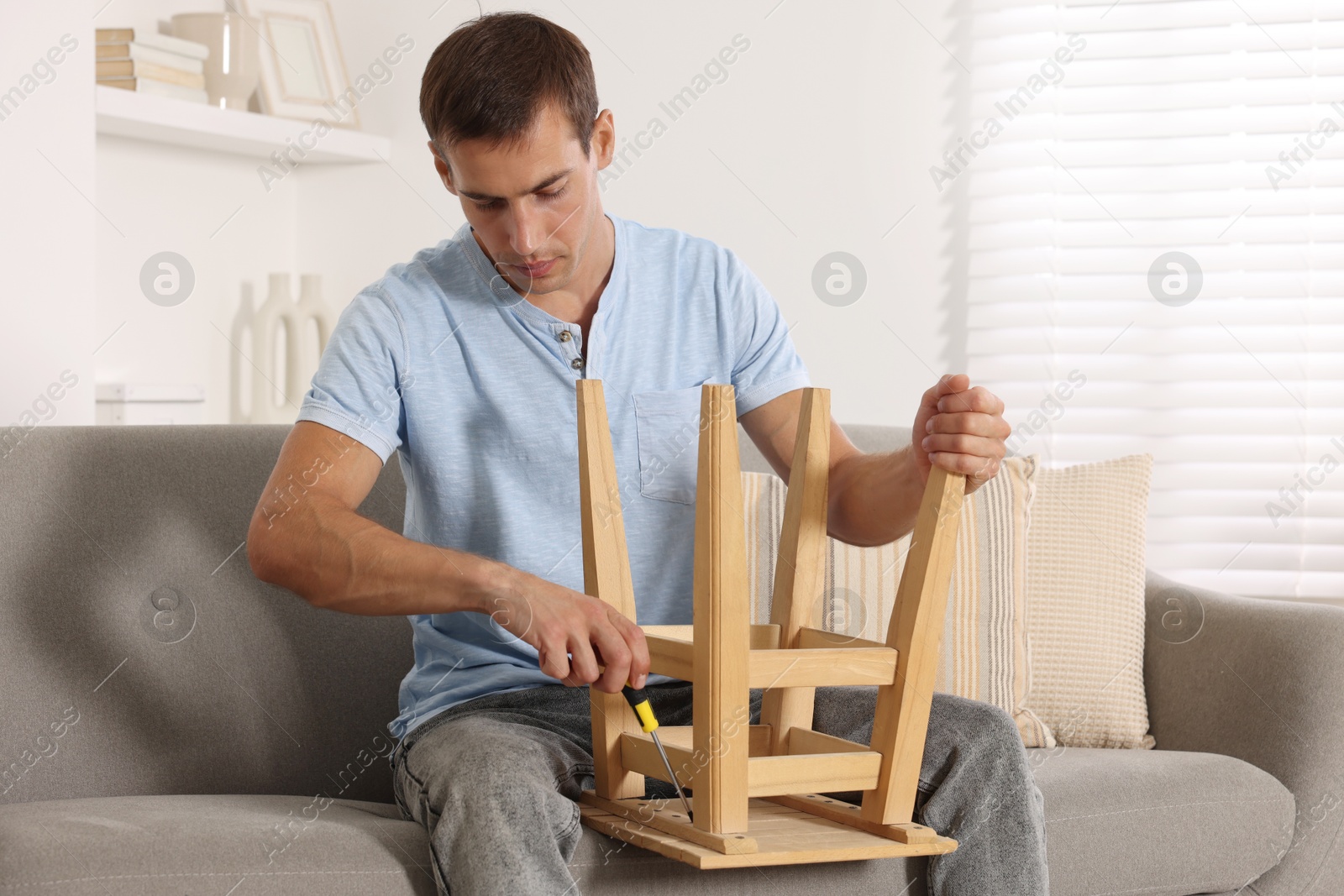 Photo of Man repairing wooden stool with screwdriver indoors