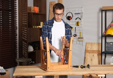 Man repairing wooden stool with screwdriver indoors