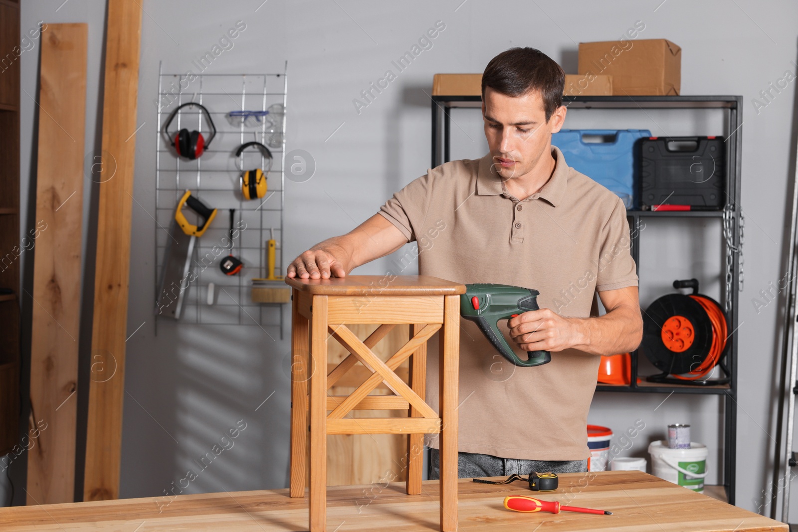 Photo of Man repairing wooden stool with electric screwdriver indoors