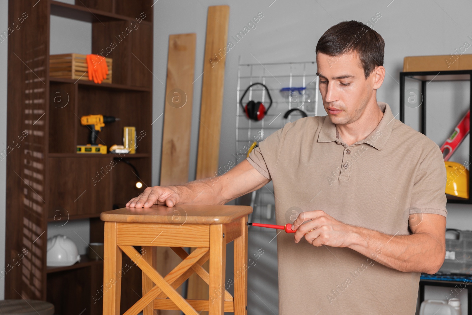 Photo of Man repairing wooden stool with screwdriver indoors