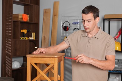 Photo of Man repairing wooden stool with screwdriver indoors