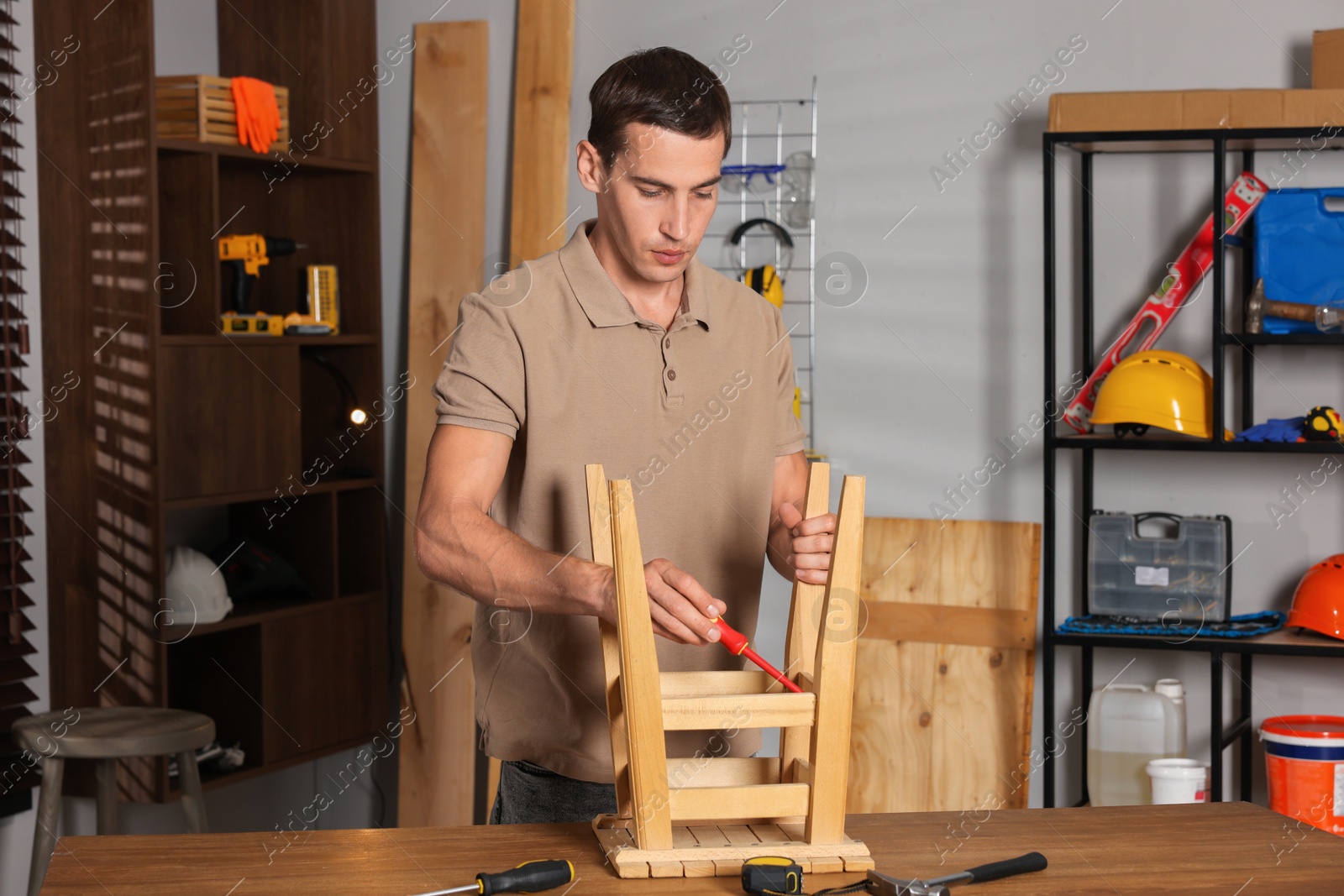 Photo of Man repairing wooden stool with screwdriver indoors