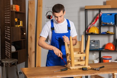 Photo of Man repairing wooden stool with screwdriver indoors