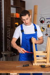 Photo of Man repairing wooden stool with screwdriver indoors