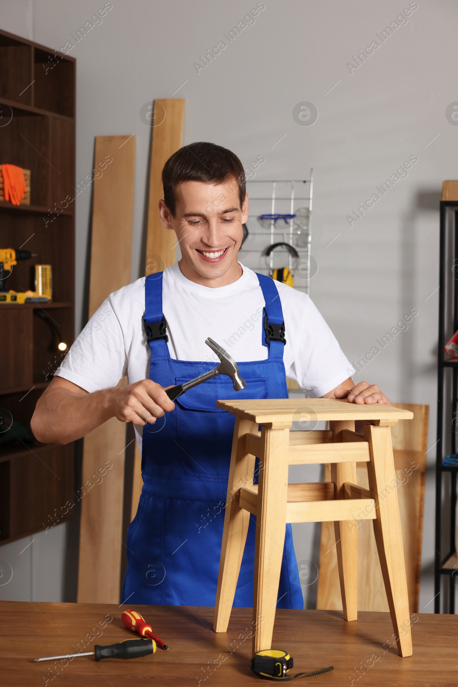 Photo of Man repairing wooden stool with hammer indoors