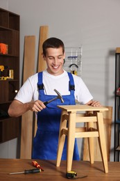 Photo of Man repairing wooden stool with hammer indoors